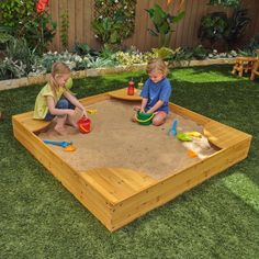 two children playing in a sandbox on the grass