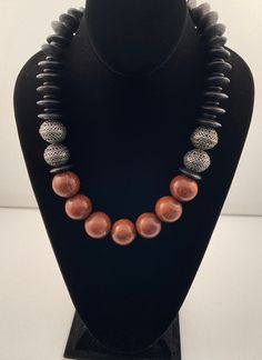 This is a very rich warm-colored necklace that looks great on black or other contrasting color.  The brown wood beads at set against the etched pewter beads and black wood spacer beads.  it is completed by an etched pewter clasp. Artisan Brown Spacer Beads, Artisan Necklace With Brown And Black Beads, Traditional Brown Jewelry With Black Beads, Unique Black Necklaces With Polished Beads, Mahogany Wooden Beads Jewelry, Vintage Black Jewelry With Wooden Beads, Mahogany Colored Wooden Bead Jewelry, Unique Brown Polished Beads, Wooden Beaded Jewelry With Round Beads