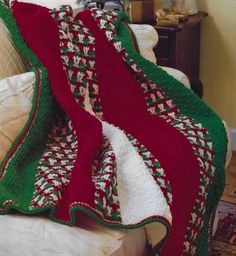 a red and green blanket sitting on top of a white couch next to a pillow