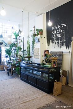 a room filled with lots of potted plants next to a wall mounted sign that says buy now or cry later