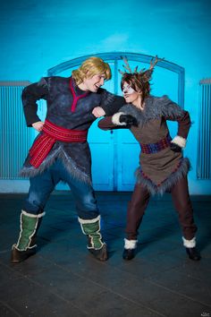 two people dressed in costumes standing next to each other on a stage with blue walls behind them