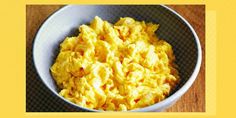 a bowl filled with scrambled eggs sitting on top of a wooden table next to a yellow frame