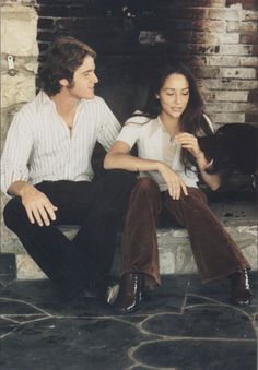 a man and woman sitting next to each other in front of a fire place with a dog