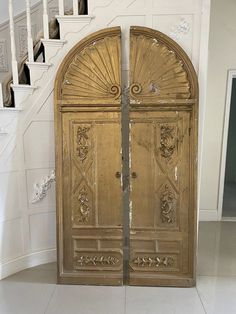 an ornate gold door in the middle of a white room with stairs leading up to it