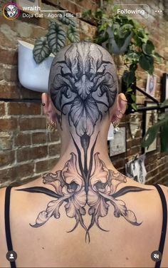 the back of a woman's head with tattoos on her neck and behind it is an image of flowers