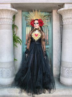 a woman in a black dress with red roses on her head standing next to a door