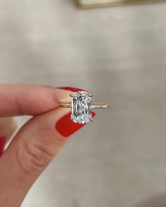 a woman's hand holding an engagement ring with a diamond in the center and a red nail polish on it