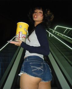 a woman holding a can of popcorn while standing on an escalator at night