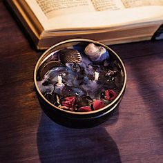 an open book on a table next to a bowl filled with rocks and seashells