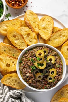 a white plate topped with olives and bread slices next to bowls of dipping sauce