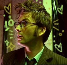 a man wearing glasses and a suit with numbers drawn on the wall behind his head