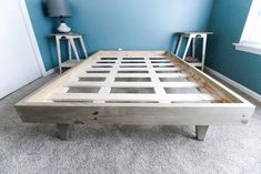 a bed frame made out of wood in a room with blue walls and white carpet