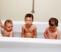 three young boys sitting in a bathtub with their hands on the edge of the tub