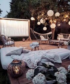 an outdoor seating area is lit up with lanterns and flowers in the foreground, surrounded by hanging lights