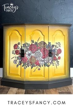 a yellow cabinet with flowers painted on it and the words trace's fancy com