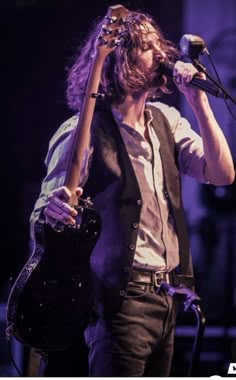 a man with long hair holding a guitar and singing into a microphone while standing on stage