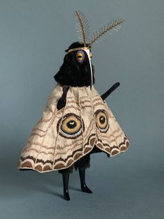 a stuffed animal is wearing a dress made out of cloths and feathers on its head