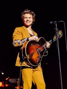 a man holding a guitar while standing in front of a microphone on top of a stage