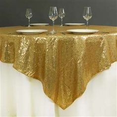 a gold table cloth with white plates and wine glasses on it, set up for a formal function