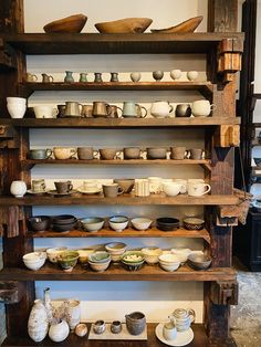 a shelf filled with lots of bowls and plates on top of wooden shelves next to a wall