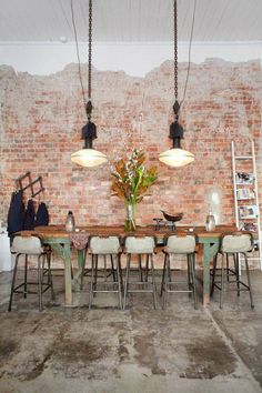 a dining room table and chairs in front of a brick wall with hanging lights above it