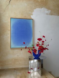 a vase filled with red flowers sitting on top of a table next to a painting