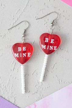 two lollipop earrings with the words be mine on them