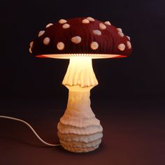 a mushroom shaped lamp is lit up on a dark surface with a white cord attached to it