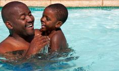 a man holding a small child in the middle of a swimming pool with blue water