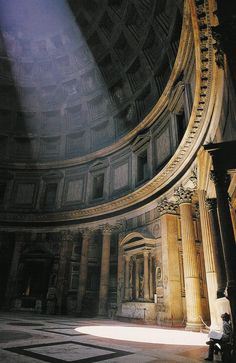 the inside of a building with columns and light coming in from the ceiling on it