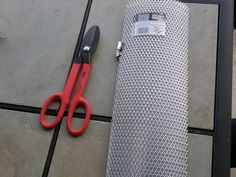 a pair of scissors sitting on top of a piece of metal mesh next to a roll of fabric