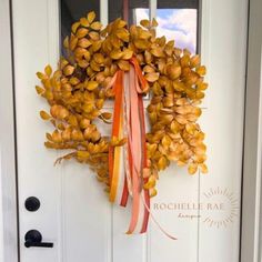 a wreath on the front door with ribbons hanging from it's sides and an orange bow