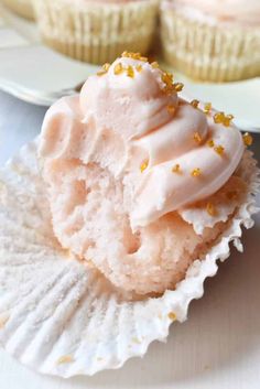 a cupcake with white frosting and gold sprinkles on a paper plate