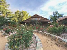 a house surrounded by flowers and trees on a sunny day