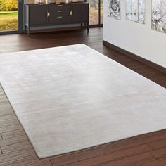 a large white rug is in the middle of a room with wood floors and windows