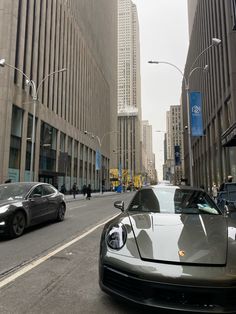 a silver sports car driving down a street next to tall buildings