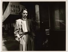 black and white photograph of a woman standing in front of a building with her hands on her hips