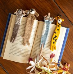 three stuffed animals laying on top of an open book with flowers in front of them