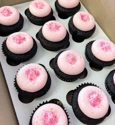 cupcakes with pink frosting and sprinkles are in a box