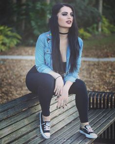 a woman sitting on top of a wooden bench in the woods with her legs crossed