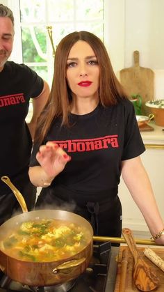 a man and woman cooking food in a pan on top of the kitchen stove together