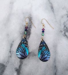 a pair of earrings with blue and green butterflies on them sitting on a marble surface