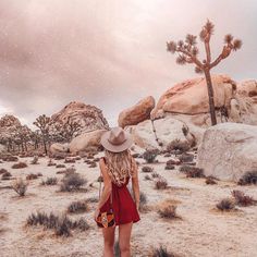 a woman standing in the desert with her back to the camera and wearing a hat