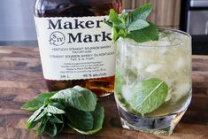 a bottle of maker's mark next to a glass filled with ice and mint