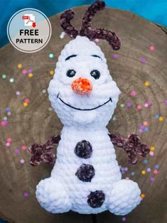 a crocheted snowman sitting on top of a piece of wood with sprinkles