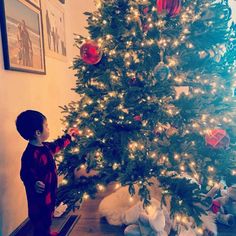 a little boy standing in front of a christmas tree