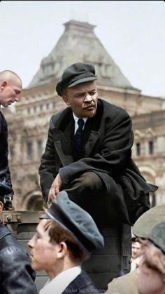 a man in a suit and hat sitting on top of a bench next to other men