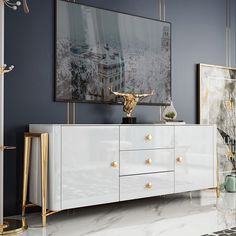 a white and gold sideboard in a living room with paintings on the wall behind it