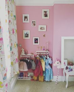 there is a pink room with pictures on the wall and clothes hanging in front of it