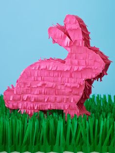 a pink paper bunny sitting in the middle of some green grass on a blue background